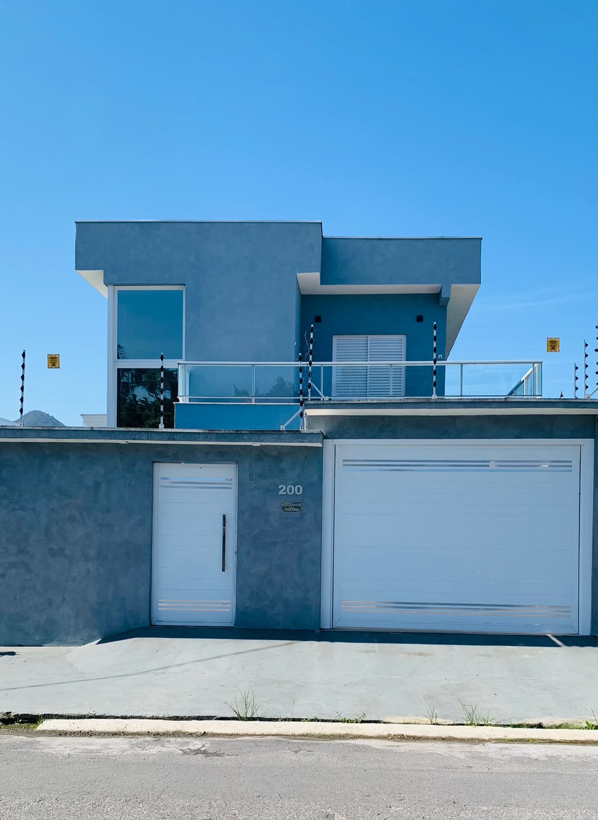 Fachada de uma residência contemporânea concluída, com acabamento azul, varanda e garagem